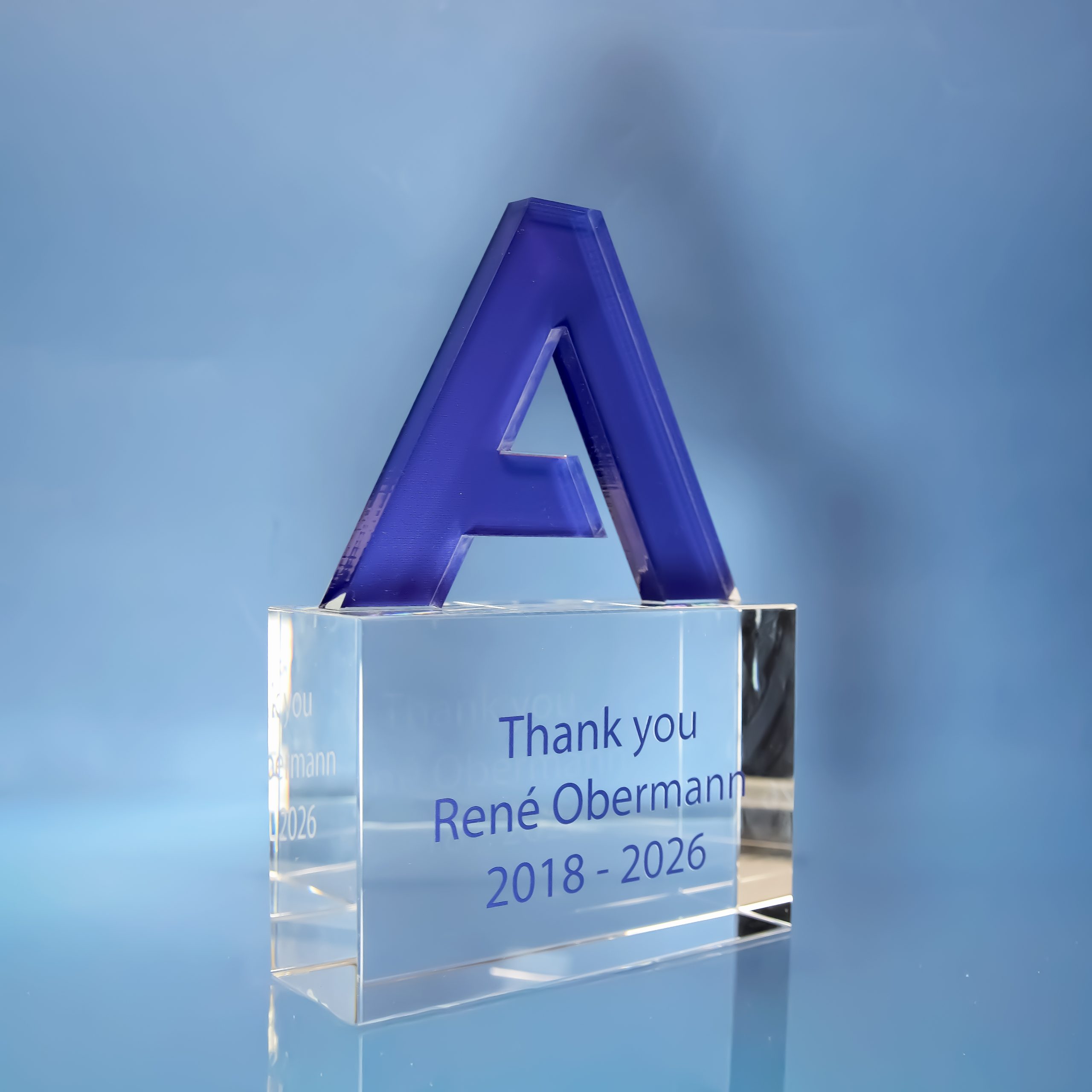 Trophée en acrylique bleu découpé au laser en forme de lettre A, sur socle en verre extra blanc imprimé en UV<br />
